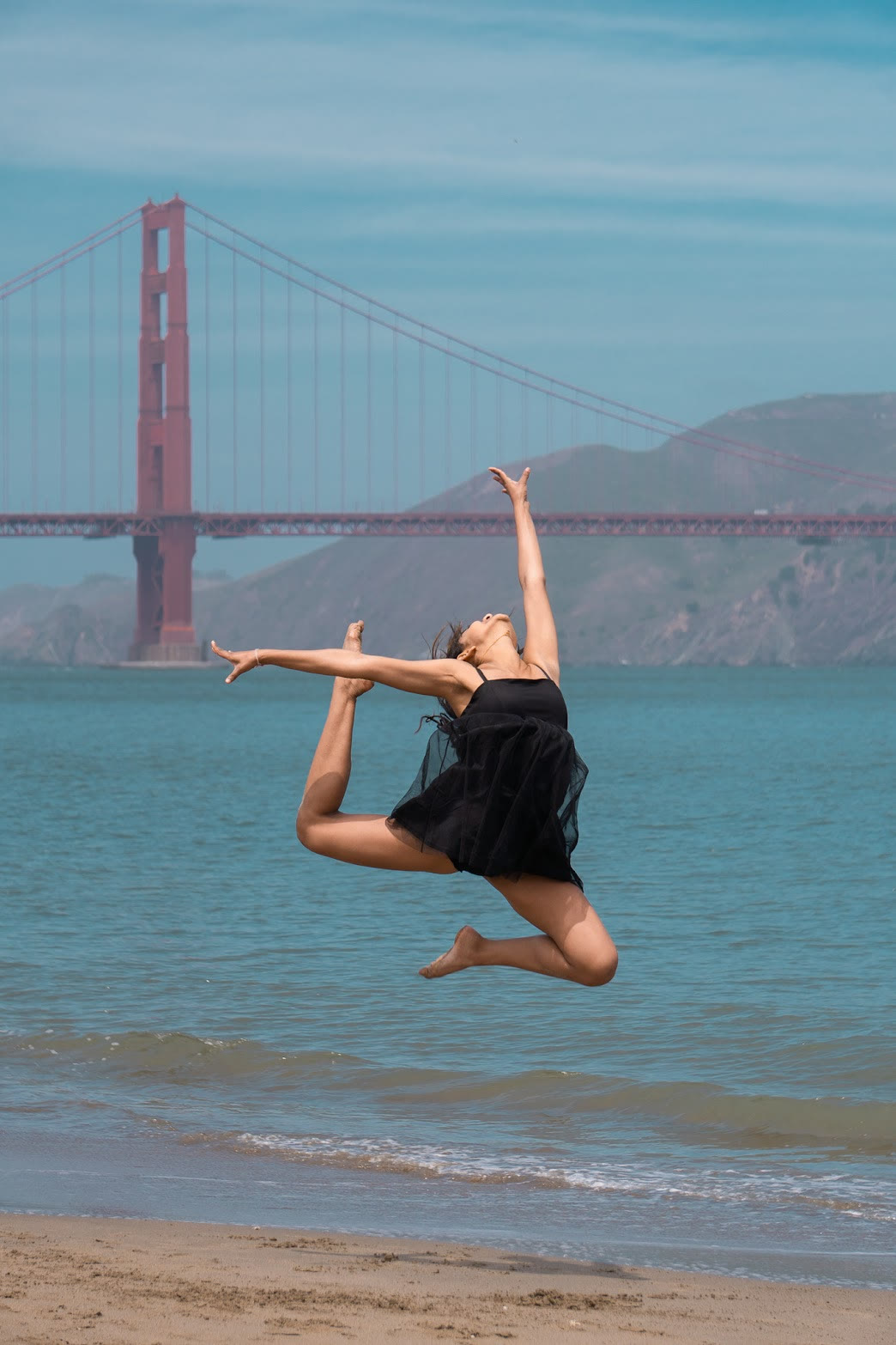 Mahika Valluri in mid-air on a San Francisco beach, Golden Gate Bridge behind her