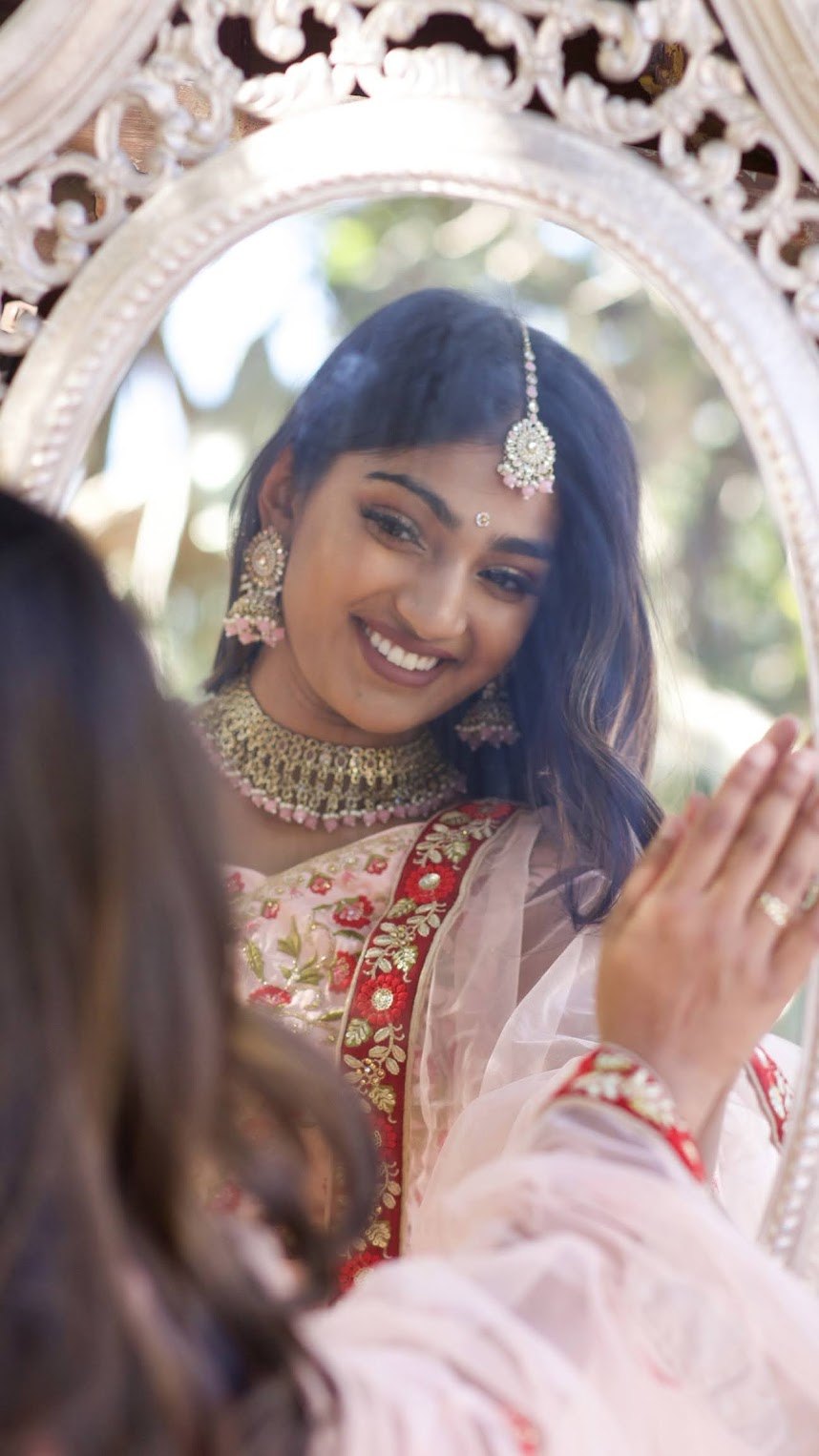 Mahika Valluri reflected in an ornate mirror, wearing a pink lehenga and traditional jewelry