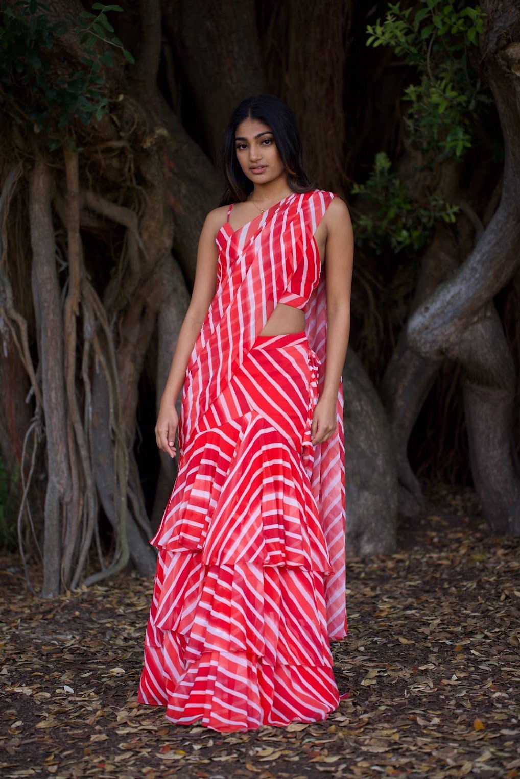 Mahika Valluri in a red and white ruffled saree among tree roots